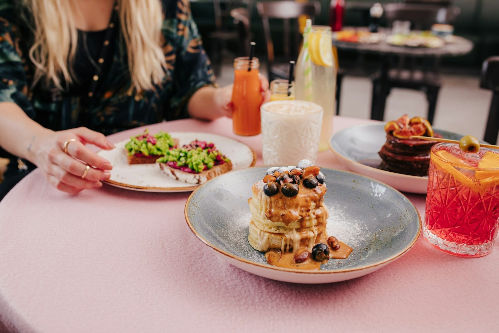 A brunch table with blueberry pancakes, avocado toast, fruit-topped pancakes, and colorful drinks