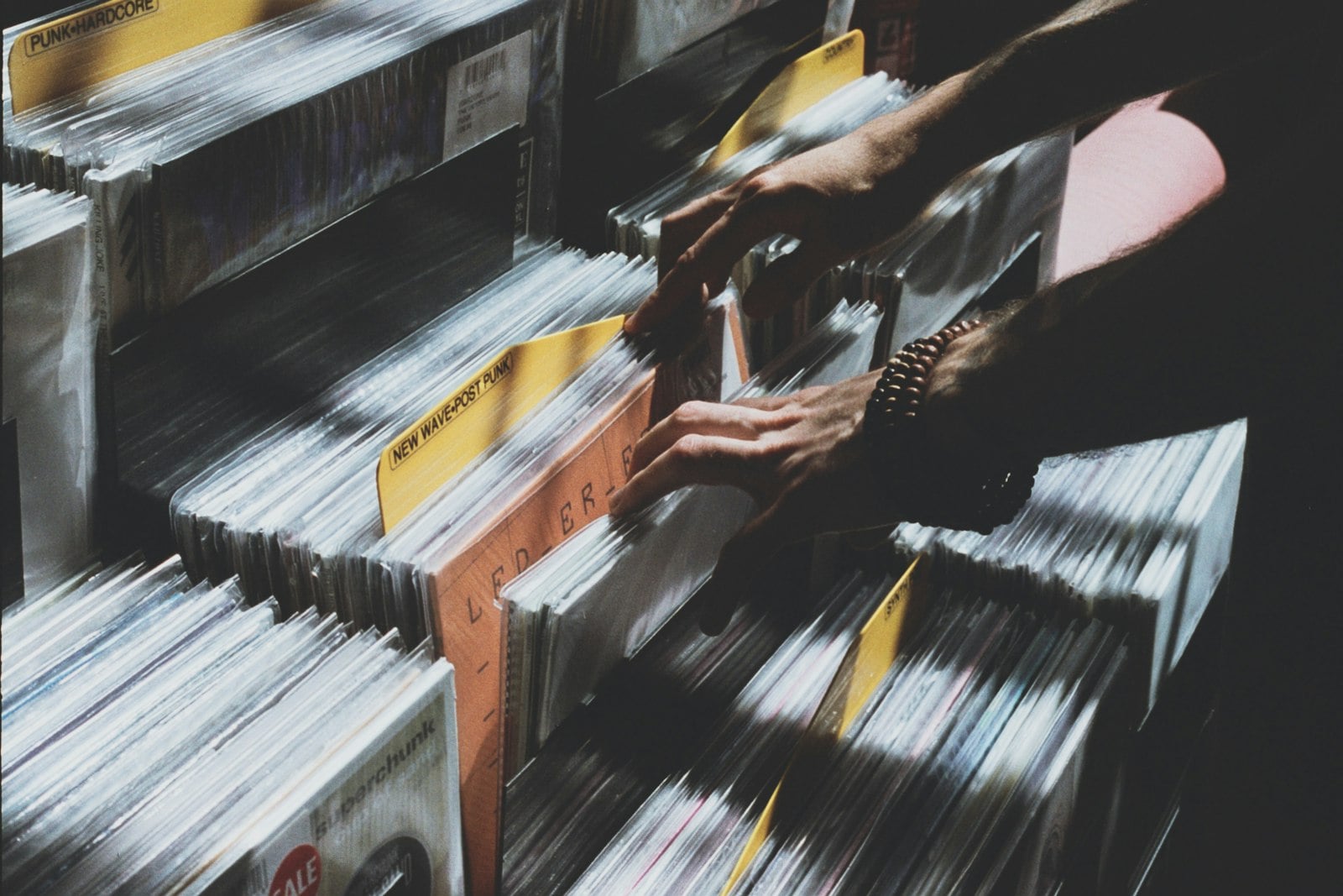 Hands lifting a record out of a crowded crate of vinyl albums
