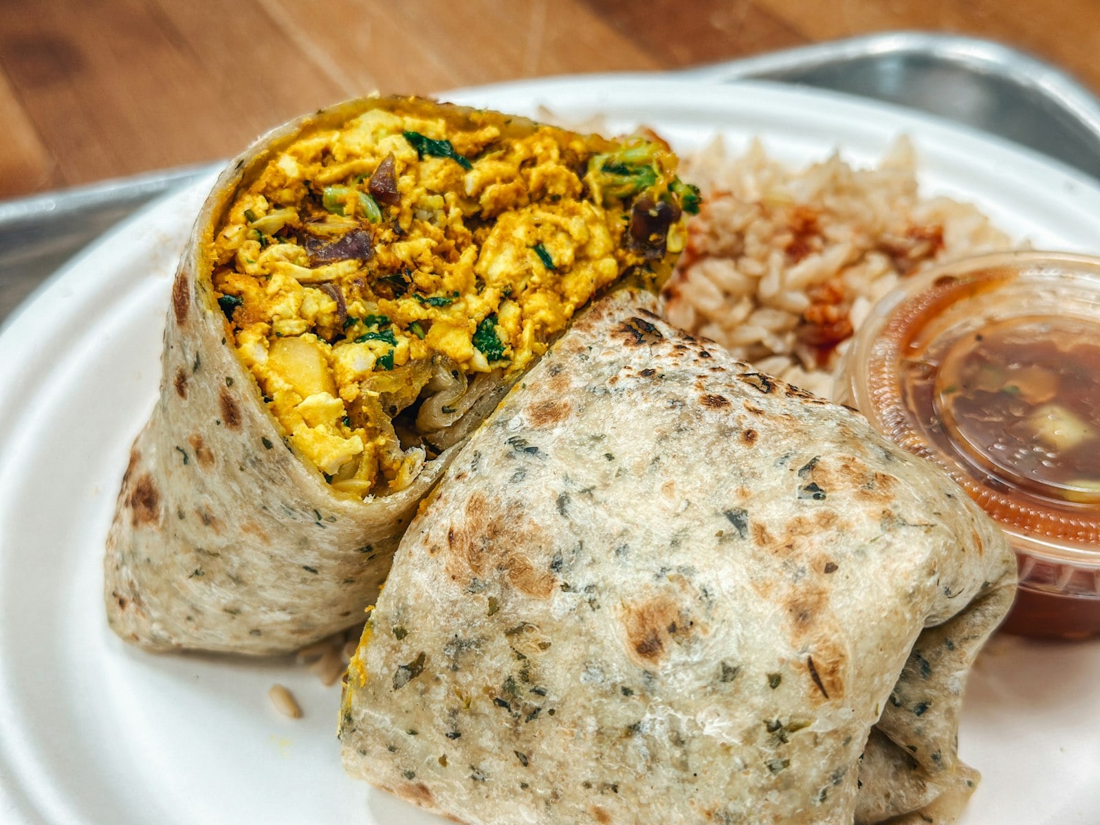 A grilled breakfast burrito cut open to show eggs, potatoes, greens, and onions
