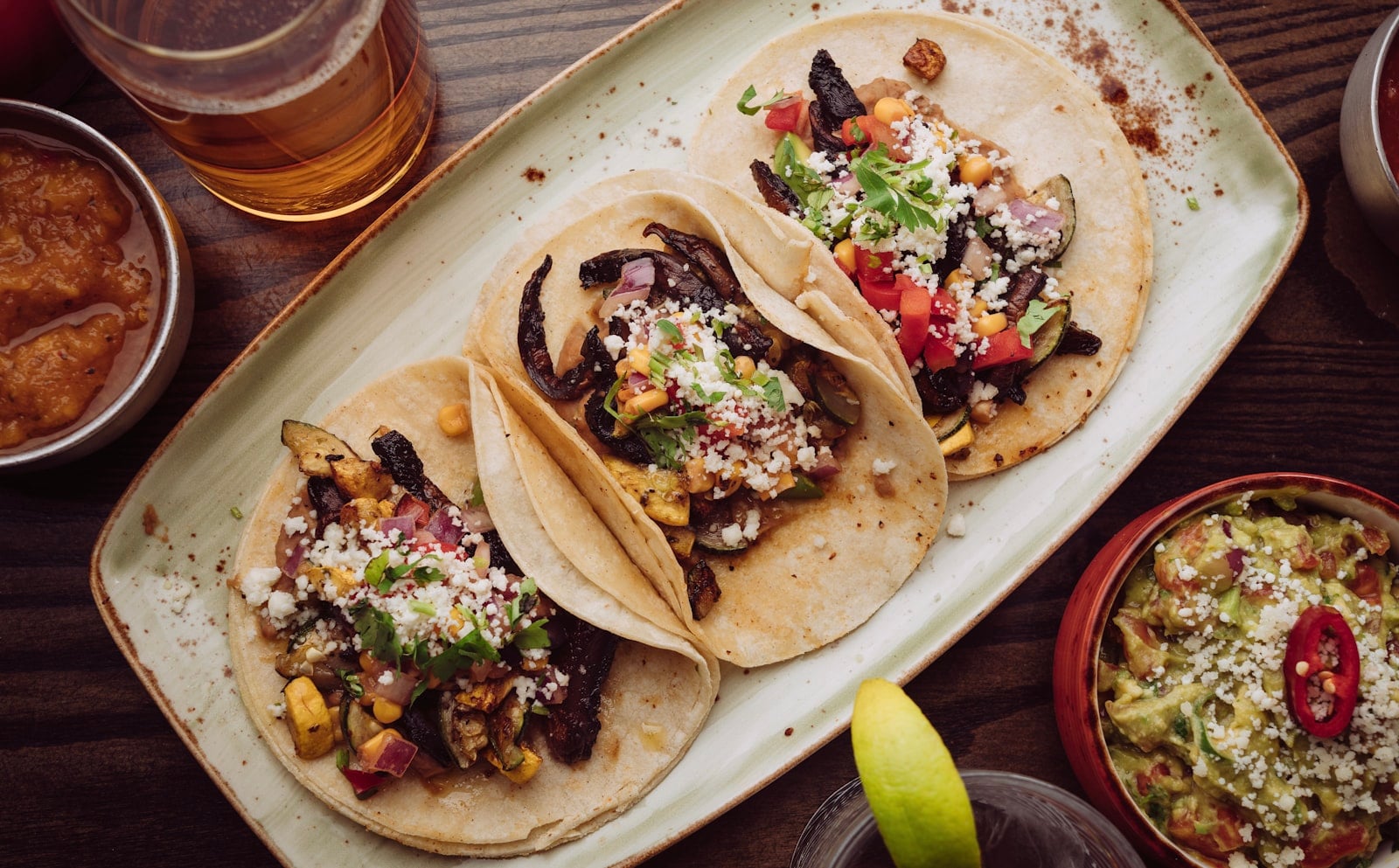 A plate of tacos with salsa, guacamole, lime, and drinks on a restaurant table