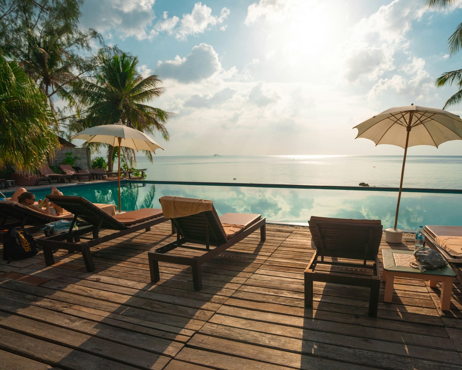 A resort swimming pool deck with loungers and palms on a bright afternoon