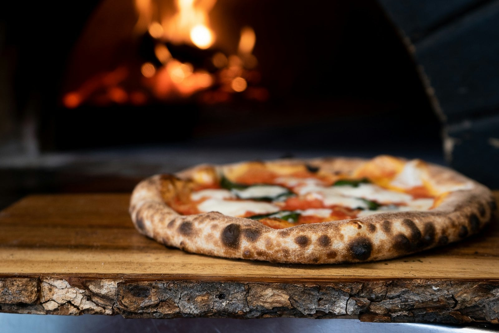 A blistered pizza with a crisp browned crust coming out of a hot oven