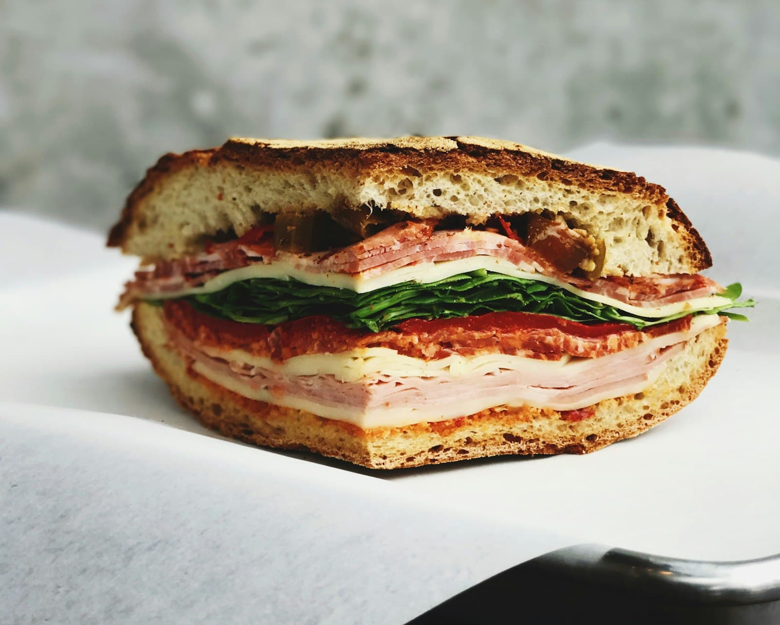 A deli sandwich stacked with sliced meat, cheese, greens, and tomato on fresh bread