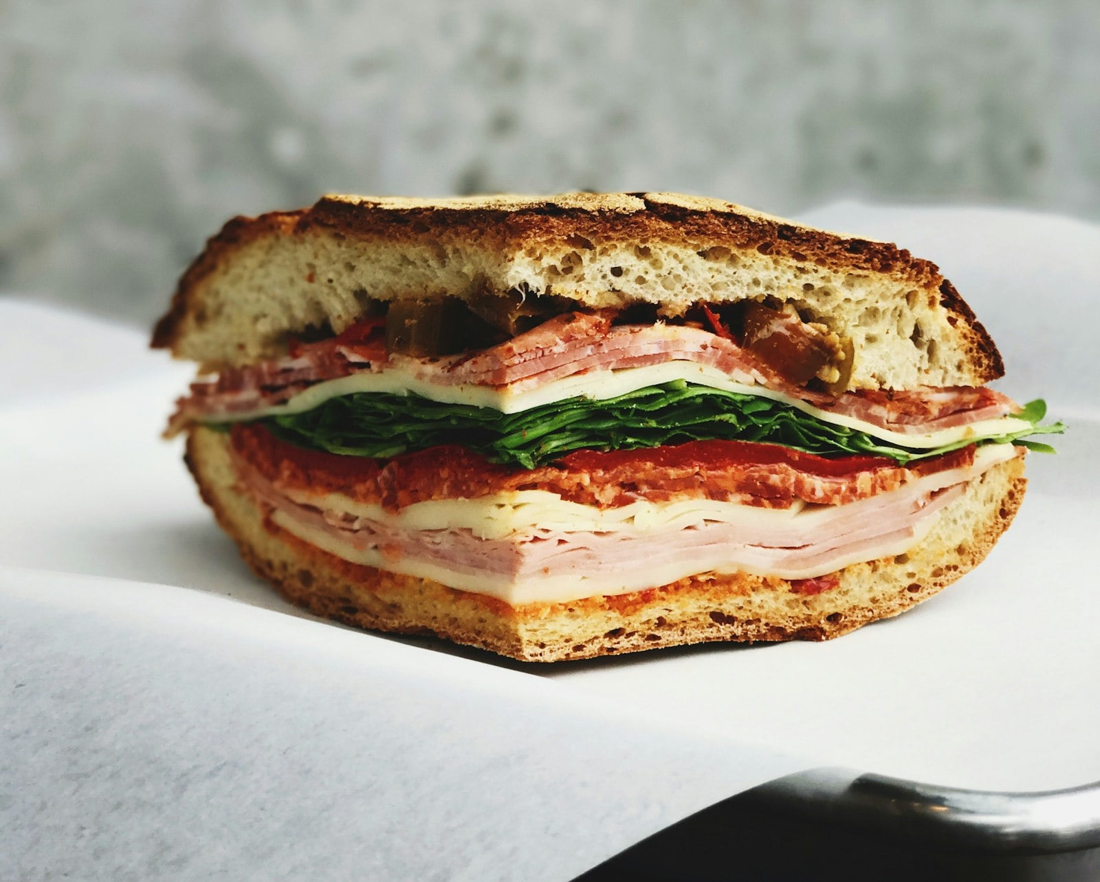 A deli sandwich stacked with sliced meat, cheese, greens, and tomato on fresh bread
