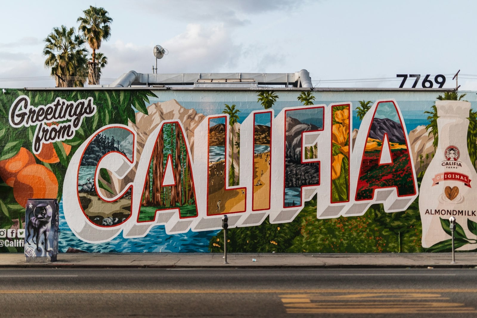 A red San Diego Trolley moving past vivid murals along the Southeast San Diego corridor