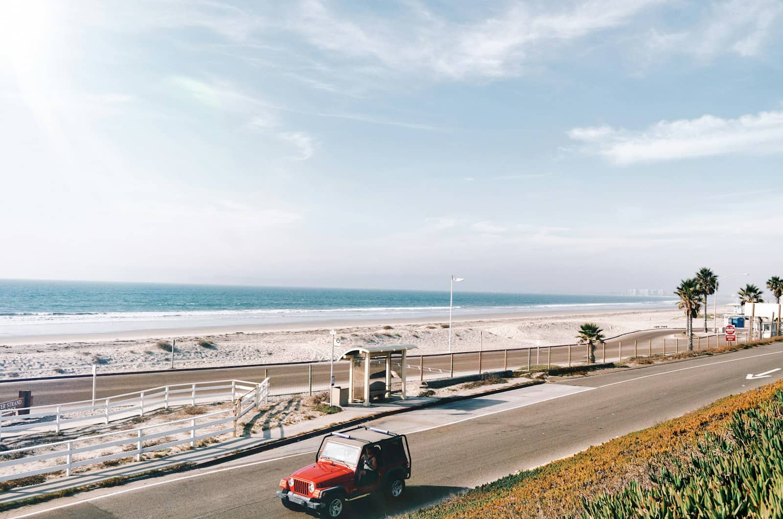 A red car on a coastal road with the ocean beyond it