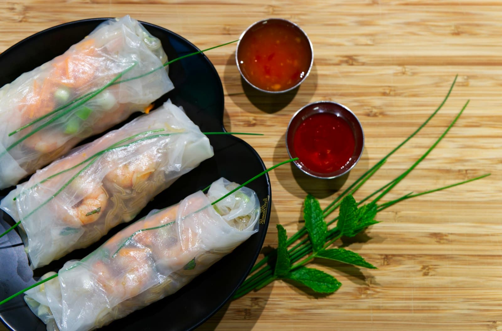 Fresh rice-paper rolls on a dark plate beside two small bowls of dipping sauce