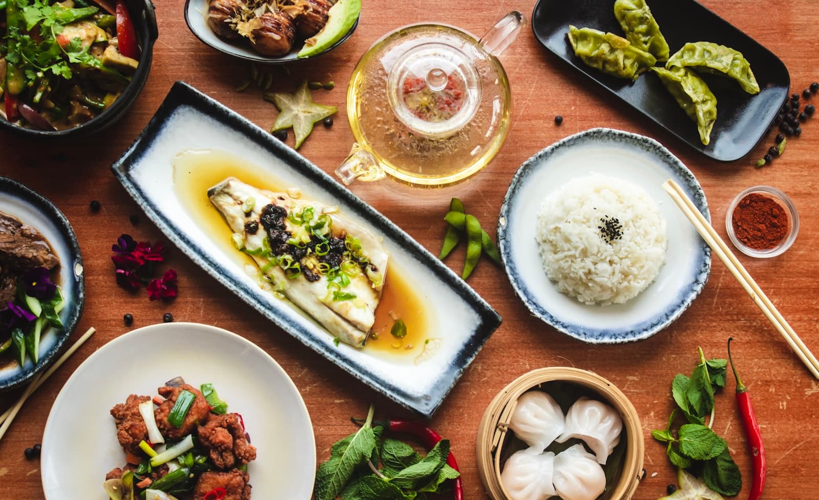 An overhead spread of Asian dishes — steamed fish, dumplings, rice and a pot of tea