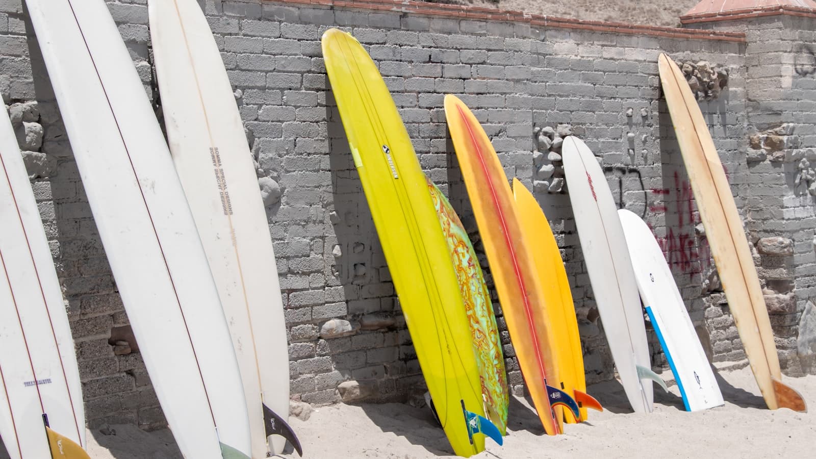 Surfboards of different shapes and colours standing upright against a whitewashed brick wall