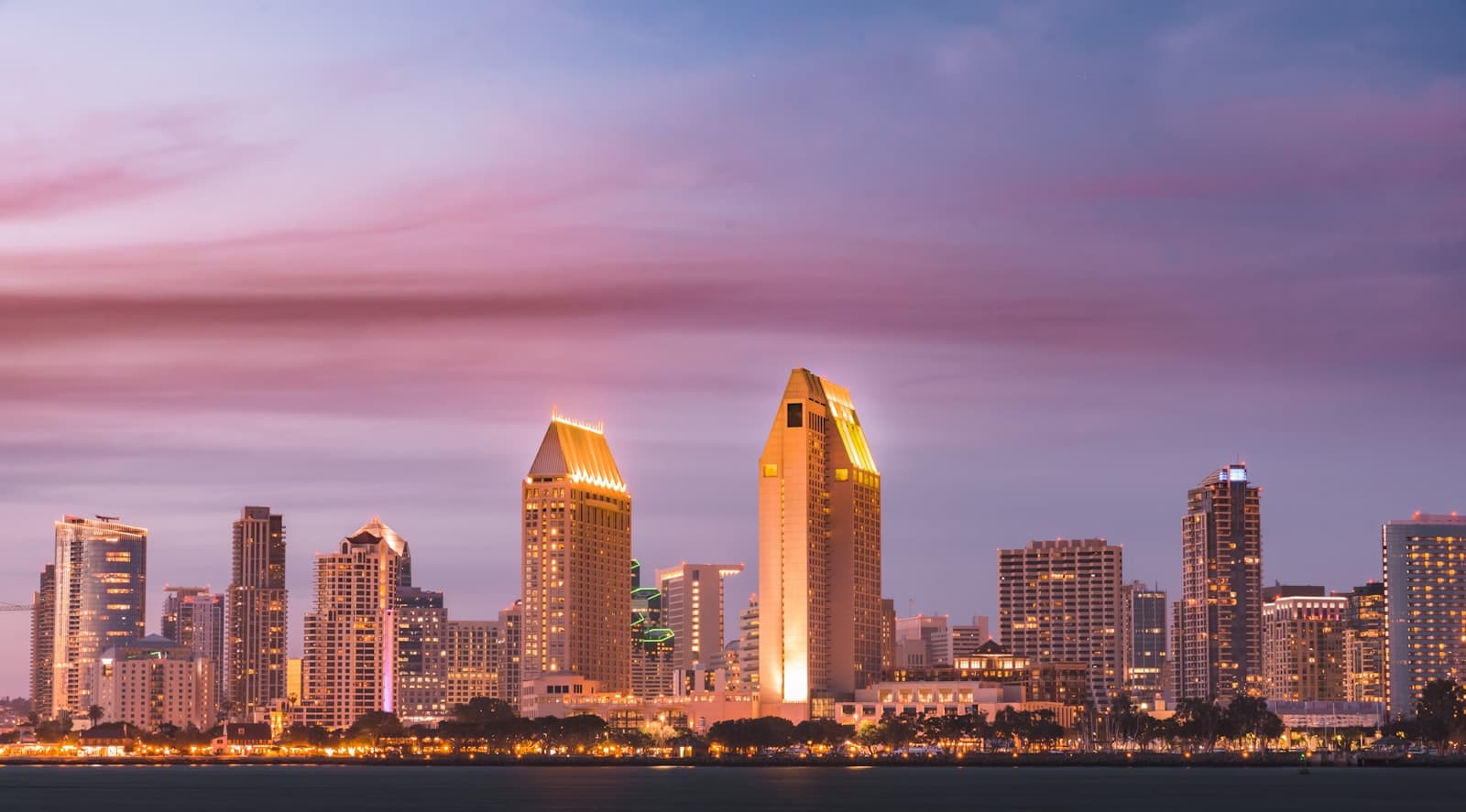 The downtown towers glowing gold against a pink and violet dusk sky