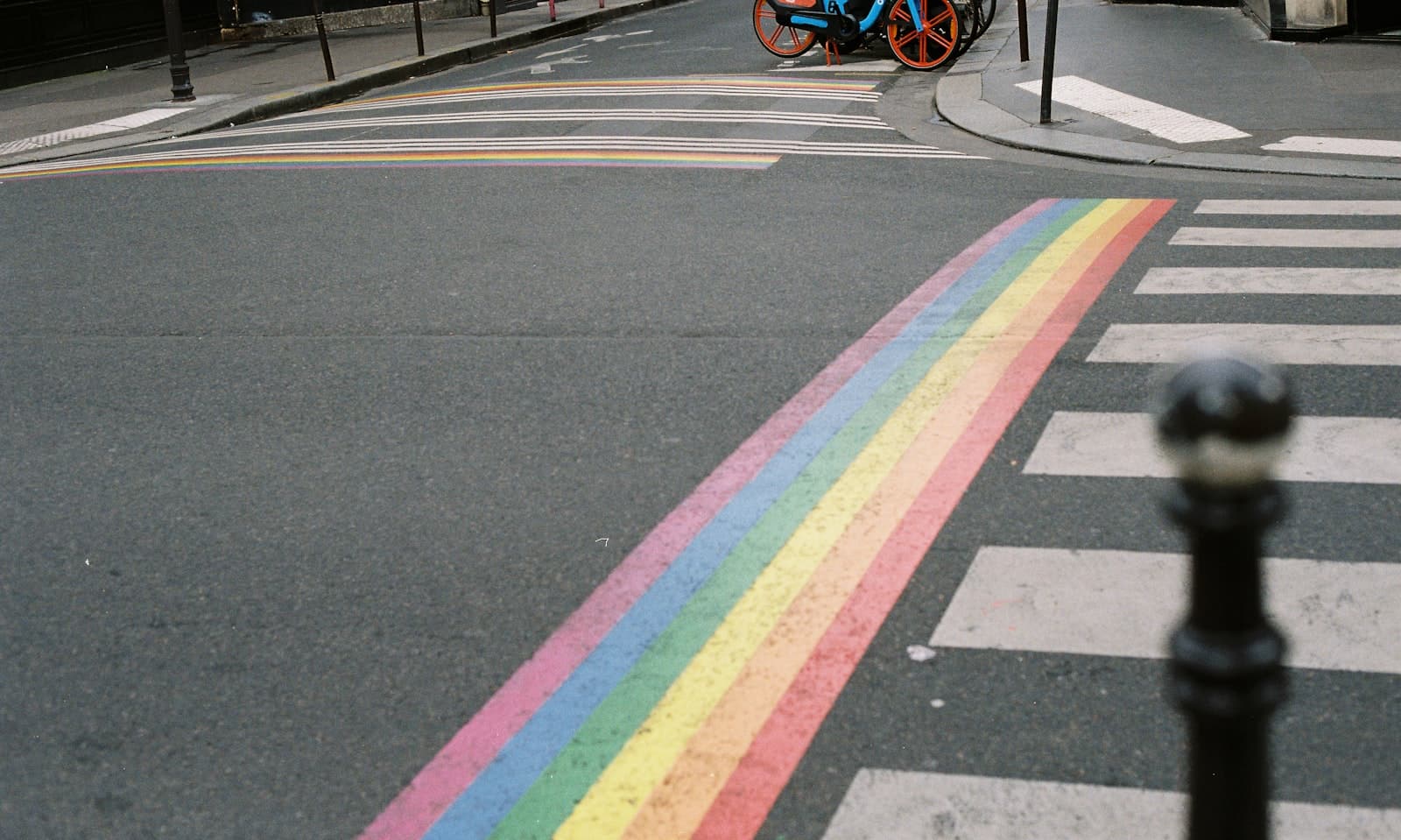 A rainbow-painted stripe running diagonally across an intersection beside a zebra crossing