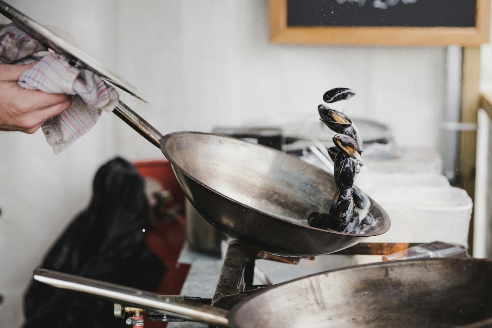 A cook tipping a steel wok over a burner in a busy kitchen