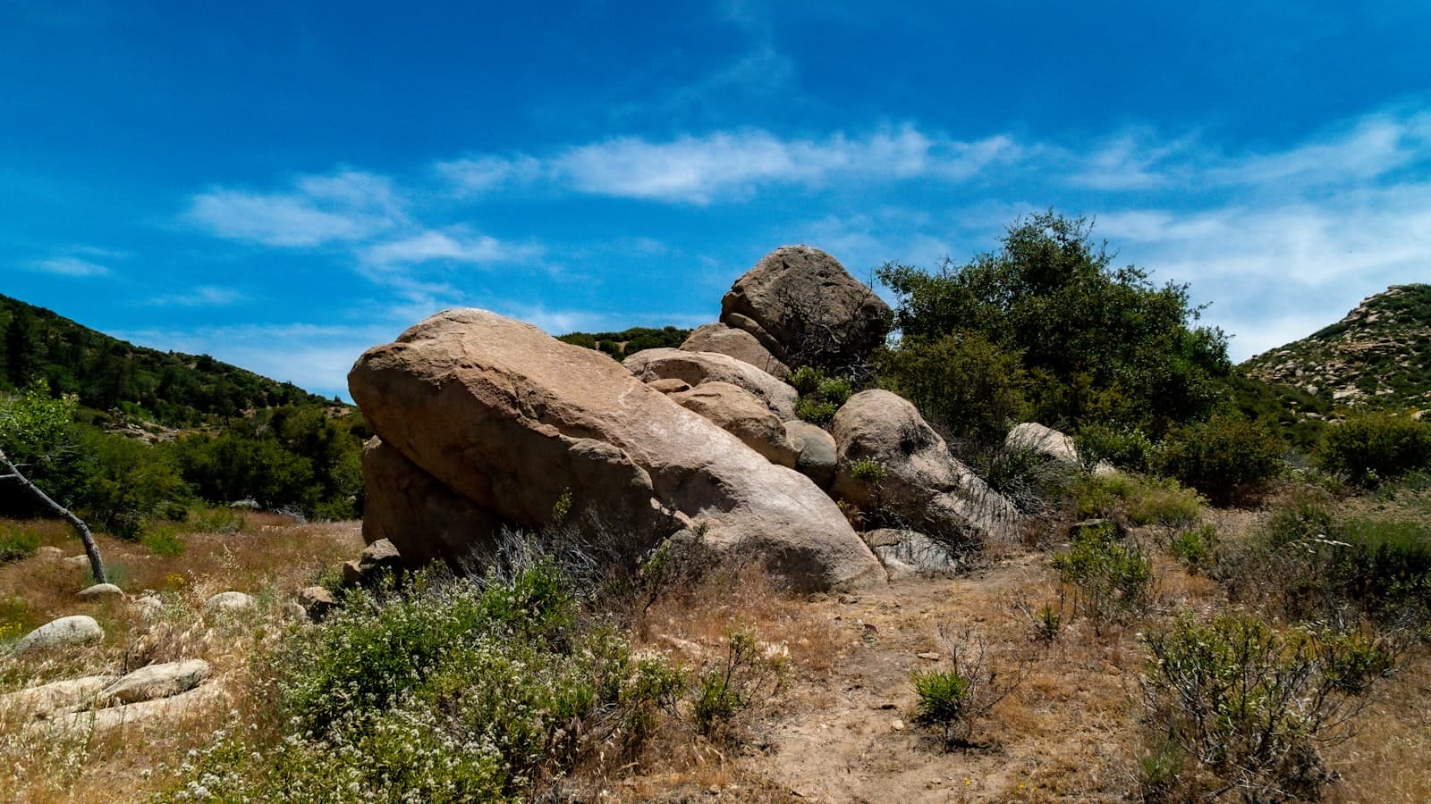 Large weathered granite boulders sitting among low chaparral under a bright blue sky