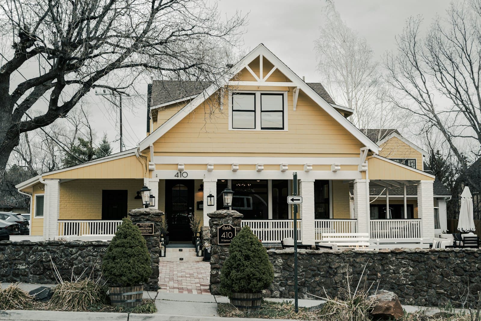 A yellow craftsman bungalow with a white porch and gabled roof behind a low stone wall